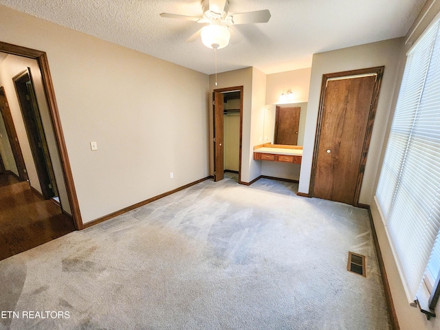 unfurnished bedroom featuring visible vents, two closets, baseboards, light carpet, and a textured ceiling