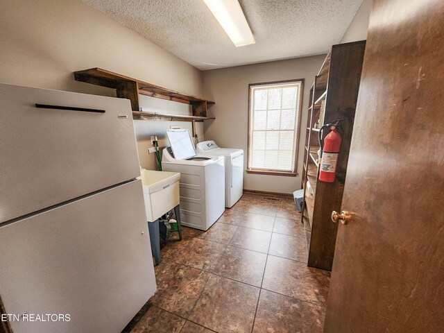 washroom with laundry area, washing machine and dryer, a textured ceiling, and baseboards