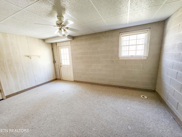 unfurnished room with carpet flooring, concrete block wall, a ceiling fan, and a drop ceiling