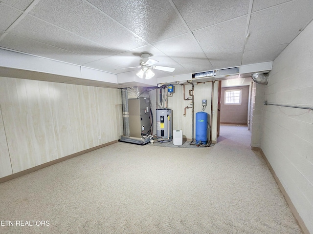 basement featuring a ceiling fan, a drop ceiling, heating unit, electric water heater, and carpet flooring