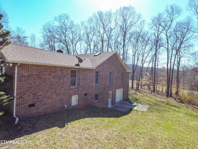 view of side of home featuring roof with shingles, a yard, a garage, crawl space, and brick siding