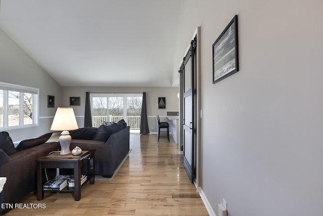 living area with baseboards, light wood-type flooring, a barn door, and vaulted ceiling