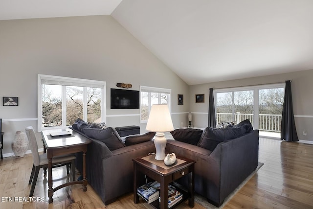 living room with baseboards, light wood-style floors, and high vaulted ceiling