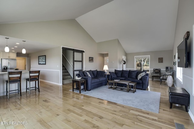 living area with light wood-type flooring, visible vents, high vaulted ceiling, and stairway