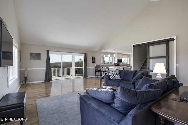 living room with a barn door, baseboards, light wood finished floors, and high vaulted ceiling