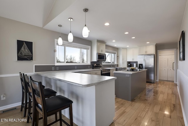 kitchen with a peninsula, appliances with stainless steel finishes, a kitchen breakfast bar, light wood-type flooring, and a center island