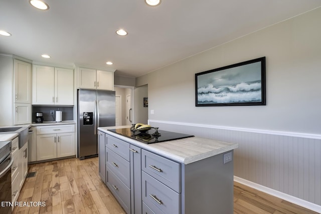 kitchen featuring a kitchen island, stainless steel refrigerator with ice dispenser, light wood finished floors, and wainscoting