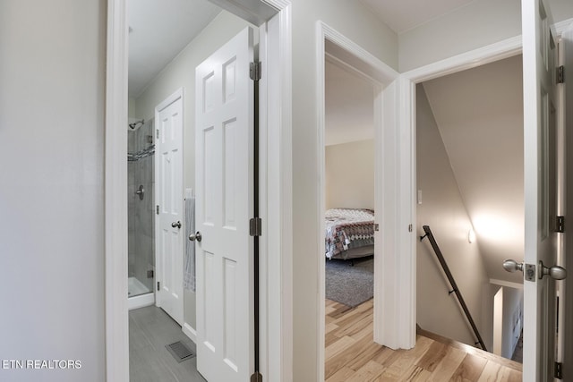 hallway with light wood-type flooring, an upstairs landing, and visible vents