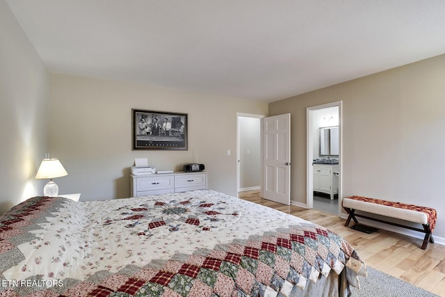 bedroom with connected bathroom, baseboards, and light wood-style floors