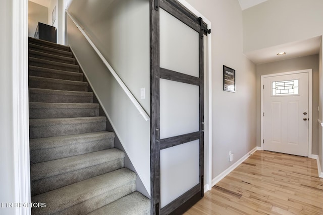 staircase with a barn door, baseboards, and wood finished floors