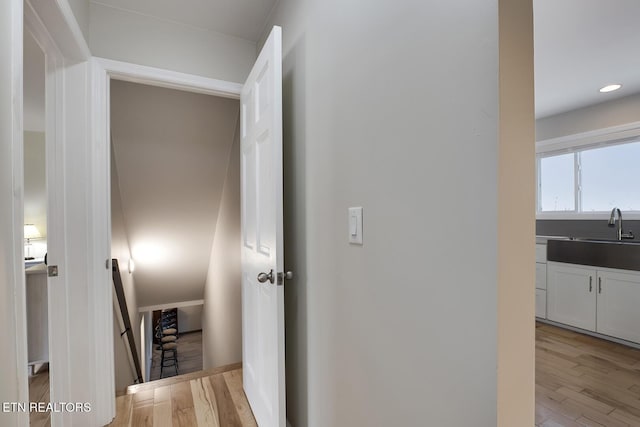 hall with recessed lighting, an upstairs landing, light wood-style floors, and a sink