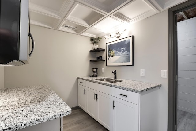 kitchen with stainless steel microwave, light stone countertops, light wood-style floors, coffered ceiling, and a sink