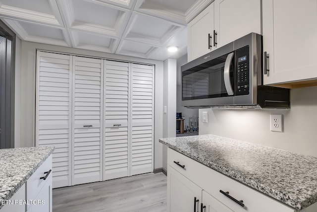 kitchen featuring light stone counters, coffered ceiling, white cabinets, stainless steel microwave, and light wood-type flooring