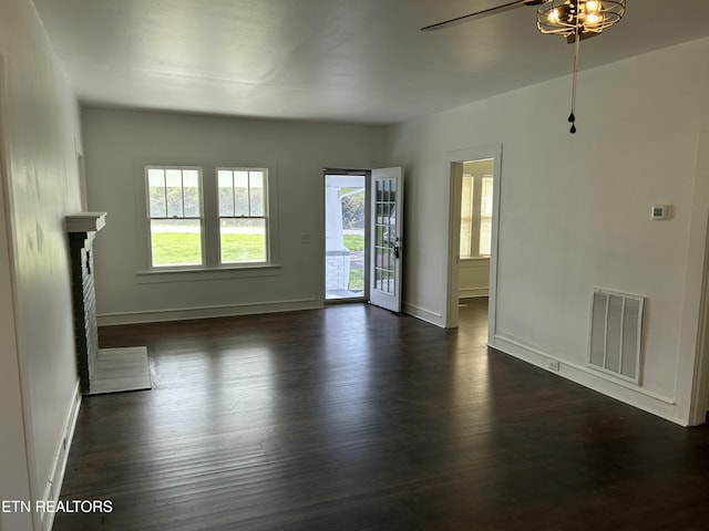 unfurnished living room featuring dark wood-style floors, visible vents, a fireplace with raised hearth, and baseboards