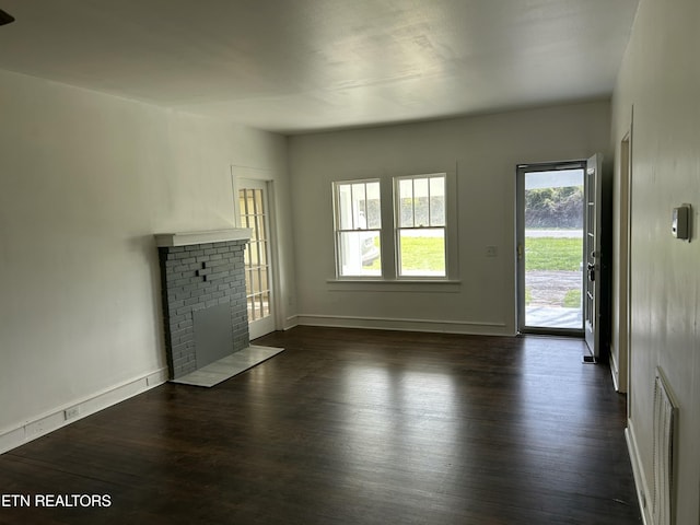 unfurnished living room with baseboards, a brick fireplace, and dark wood-style flooring