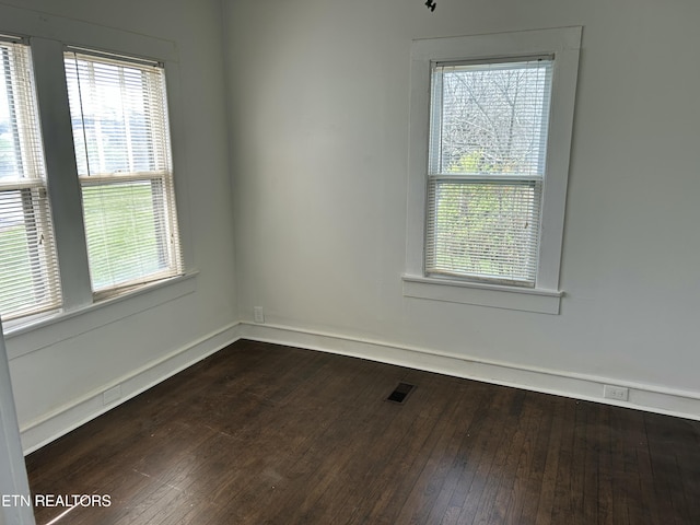 unfurnished room featuring dark wood-style floors, visible vents, and baseboards