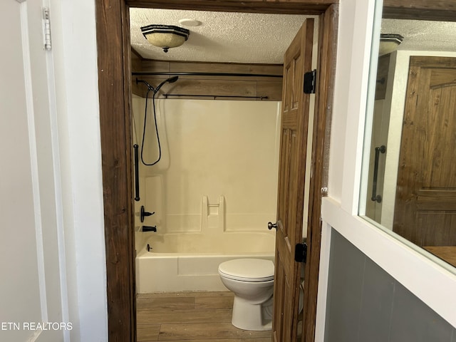 bathroom featuring toilet, a textured ceiling, shower / bathtub combination, and wood finished floors