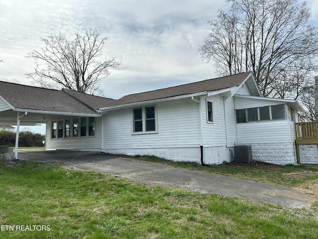 view of side of property with aphalt driveway, central air condition unit, a yard, and a shingled roof