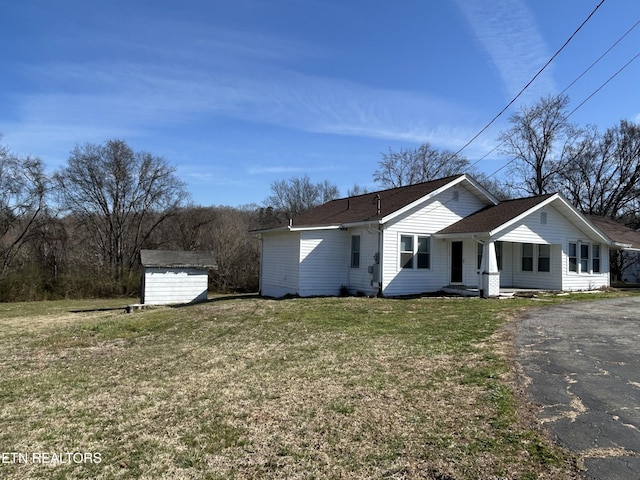 view of front of house featuring an outbuilding, a storage unit, a front yard, and a shingled roof