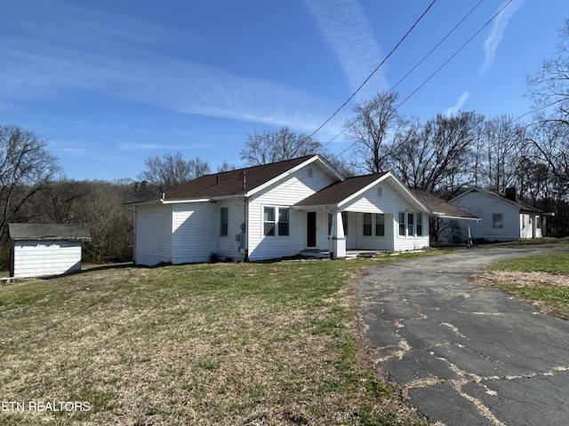 view of front of house featuring a front yard, a storage unit, an outdoor structure, and aphalt driveway