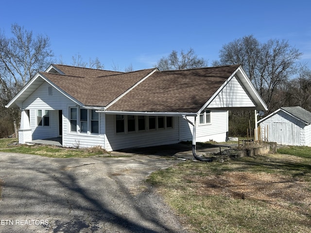 view of front facade with an outbuilding, a storage unit, driveway, and roof with shingles