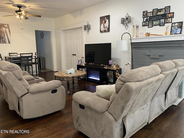 living room featuring a ceiling fan, dark wood-type flooring, and a lit fireplace