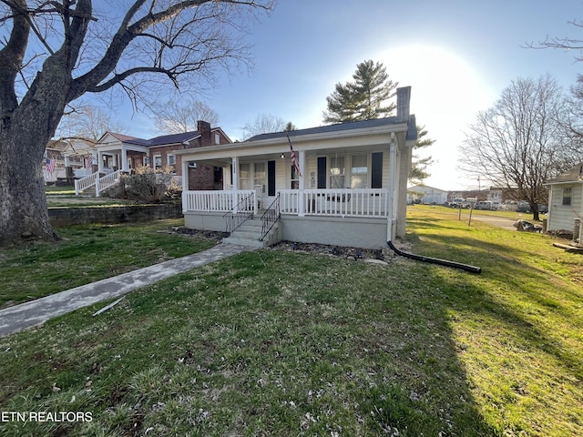 bungalow-style home featuring a front yard, covered porch, and a chimney