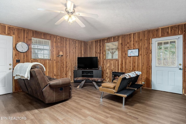 living area with wooden walls, a textured ceiling, a ceiling fan, and light wood finished floors