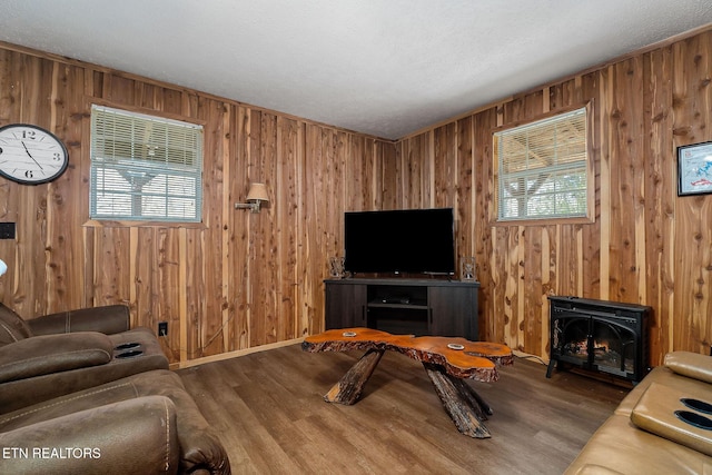 living room with wooden walls, wood finished floors, a wood stove, and a textured ceiling