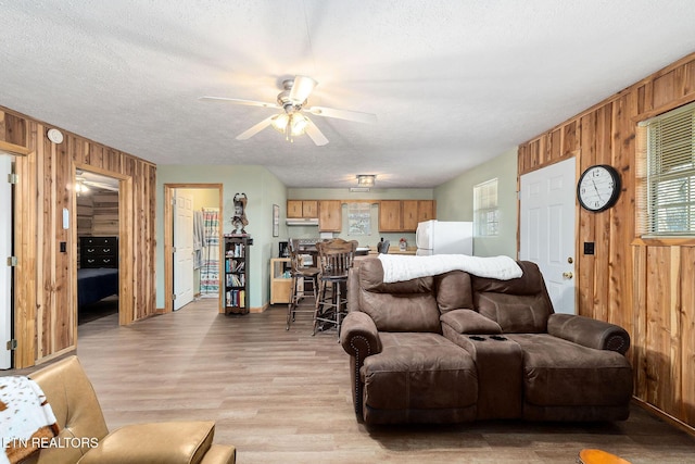 living area with light wood-style flooring, a ceiling fan, wood walls, and a textured ceiling