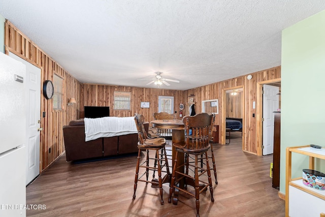 dining space featuring wooden walls, a textured ceiling, wood finished floors, and a ceiling fan