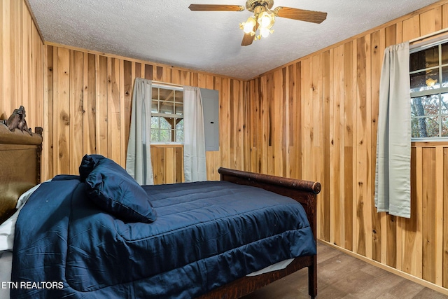 bedroom featuring wood finished floors, wood walls, a textured ceiling, and multiple windows