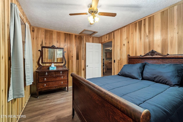 bedroom with a ceiling fan, a textured ceiling, light wood-style floors, wood walls, and attic access