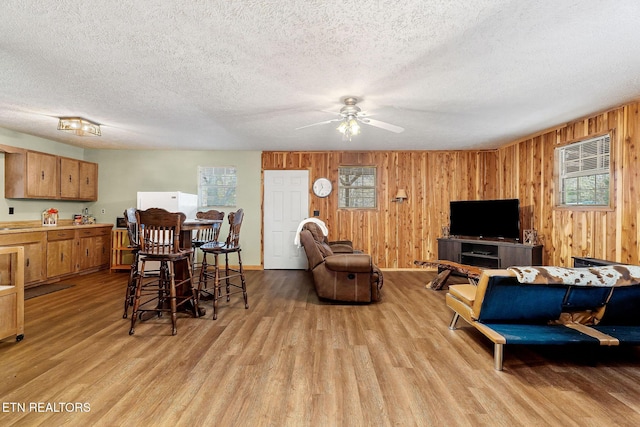 living room with ceiling fan, light wood-type flooring, wood walls, and a textured ceiling