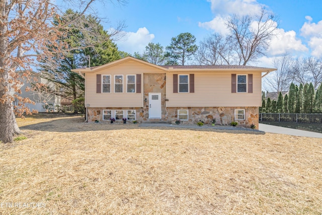 bi-level home featuring stone siding, a front yard, and fence