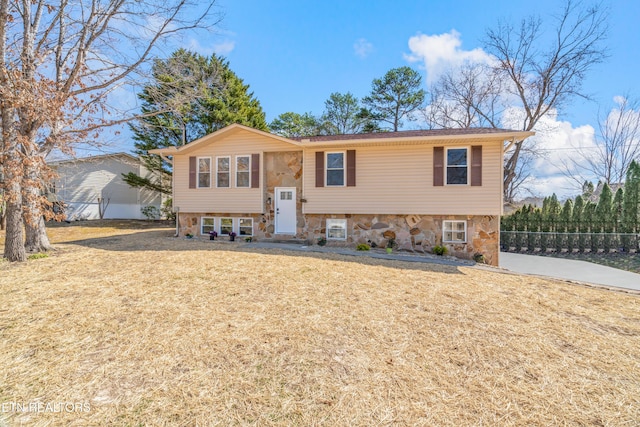 split foyer home with a front lawn, fence, and stone siding