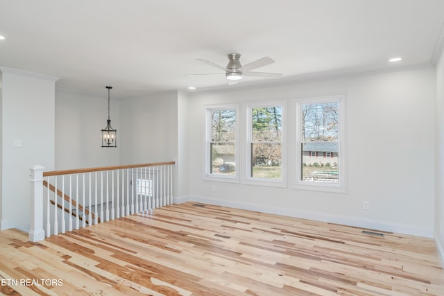 empty room with baseboards, wood finished floors, ornamental molding, and ceiling fan with notable chandelier