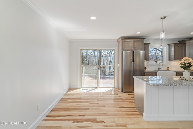 kitchen with light stone counters, light wood finished floors, freestanding refrigerator, crown molding, and tasteful backsplash