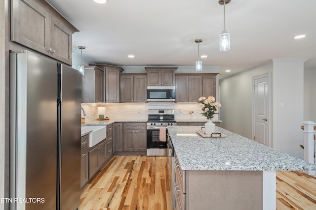 kitchen with light wood-style flooring, a sink, a kitchen island, stainless steel appliances, and decorative backsplash