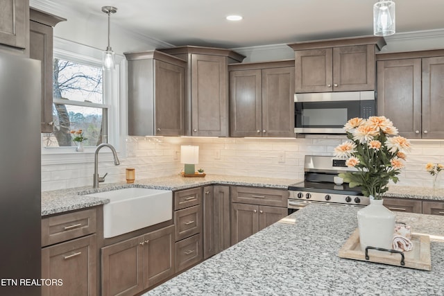 kitchen featuring a sink, hanging light fixtures, ornamental molding, stainless steel appliances, and tasteful backsplash