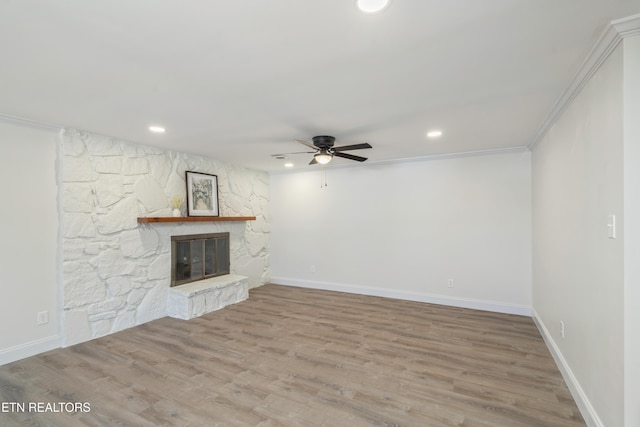 unfurnished living room with wood finished floors, baseboards, ceiling fan, a stone fireplace, and crown molding