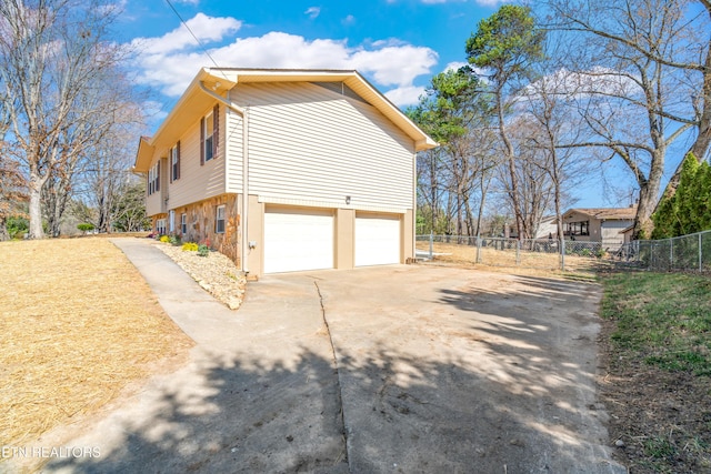 view of side of property with stone siding, concrete driveway, an attached garage, and fence