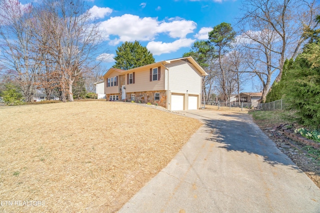 split foyer home with a garage, stone siding, concrete driveway, and fence