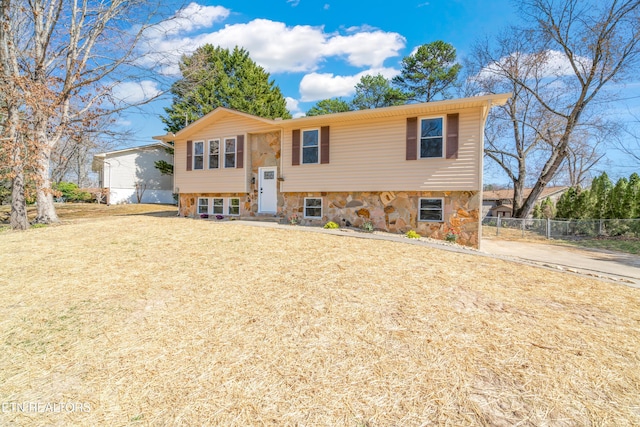 split foyer home featuring stone siding, entry steps, a front lawn, and fence