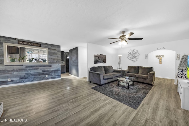 living room featuring a textured ceiling, an accent wall, a ceiling fan, and wood finished floors