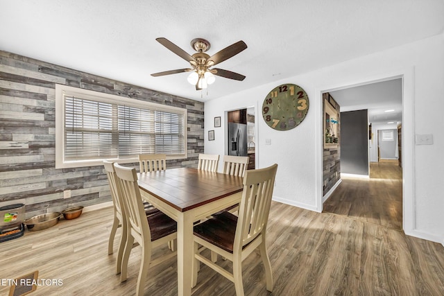 dining area with baseboards, wooden walls, wood finished floors, and a ceiling fan