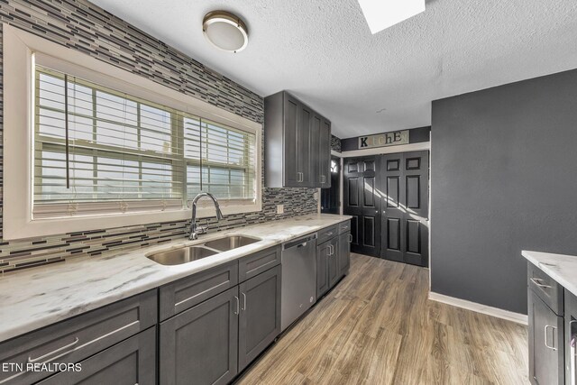kitchen with baseboards, light wood-style flooring, a sink, dishwasher, and backsplash