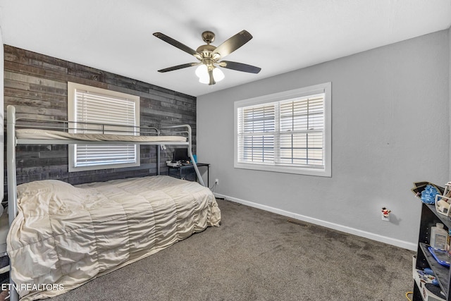 bedroom with baseboards, wooden walls, ceiling fan, and carpet flooring