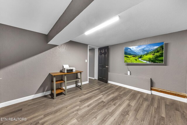 interior space featuring a textured wall, baseboards, and wood finished floors