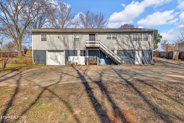 back of property with stairway, an attached garage, driveway, and fence